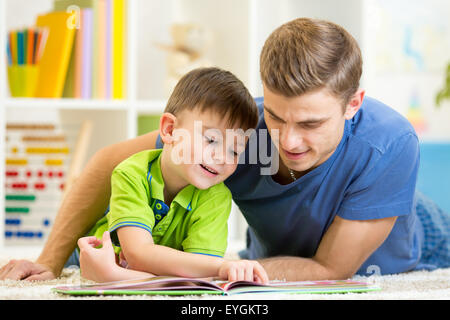 Father and son read together sitting on the floor. Kid reading story book with his dad at home. Stock Photo