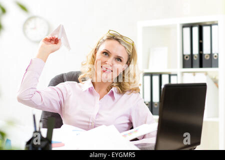 Middle-aged businesswoman throwing paper airplane in office Stock Photo
