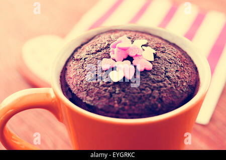 closeup of a chocolate mug cake topped with heart-shaped confetti sprinkles placed on a set table, with a filter effect Stock Photo