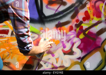 A graffiti artist working on a colourful wall mural. he's holding a tin of Kobra paint spray to finish off a tag Stock Photo