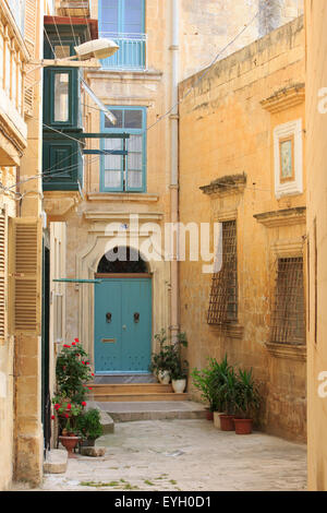 Narrow street with a limestone house with a colorful traditional closed wooden balcony and door with metal lion door knockers in Valletta, Malta Stock Photo