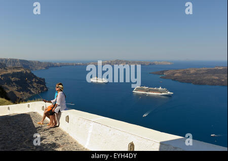 A young couple taking a Selfie photograph of themselves two with cruise ships in the distance, Santorini, Greece.