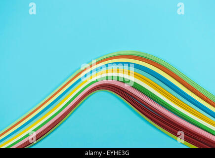 Thin colored paper ribbons forming a wave or a rainbow shape , against an azure background Stock Photo