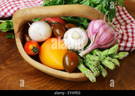 asparagus, tomatoes, garlic, mushrooms in a basket on a wooden background Stock Photo