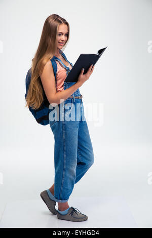 Full length portrait of a female student with backpack reading book isolated on a white background Stock Photo