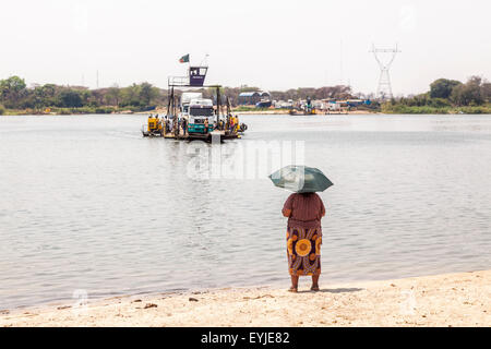 Local woman with umbrella waits for the approaching Kazungula Ferry, a pontoon ferry over the Zambezi River crossing between Botswana and Zambia Stock Photo