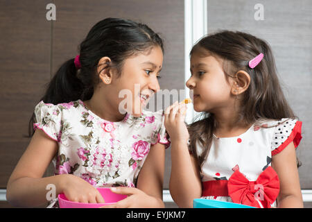 Eating traditional snack murukku. Cute Indian Asian girls enjoying food. Beautiful children model at home. Stock Photo