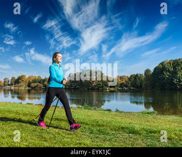 Nordic walking adventure and exercising - young woman hiking with nordic walking poles in park along river Stock Photo