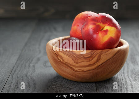 nectarines in olive wood bowl on oak table Stock Photo
