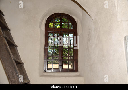 Old window with iron grid on medieval building wall with wooden ladder beside it Stock Photo