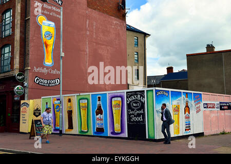 People walking past billboards advertising alcohol outside a pub in Londonderry (Derry), Northern Ireland Stock Photo