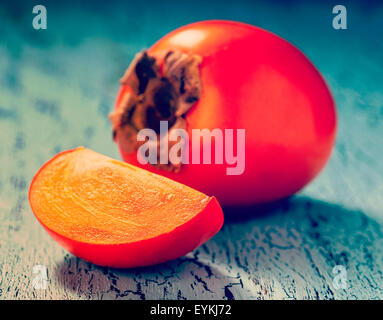 Vintage retro effect filtered hipster style image of fresh ripe persimmon with slice on a blue wooden background Stock Photo