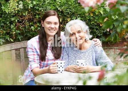 Teenage Granddaughter Relaxing With Grandmother In Garden Stock Photo