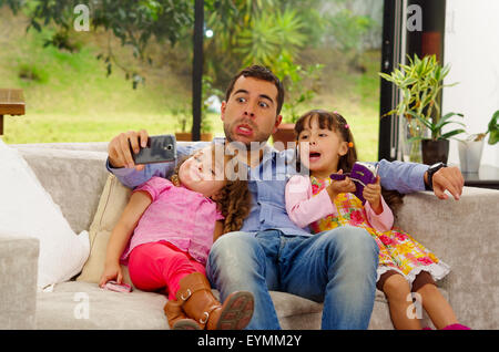 Family portrait of father and two daughters sitting together in sofa posing for selfie making funny faces Stock Photo