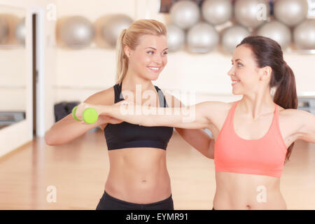 Coach helping young woman to train with TRX straps in gym Stock