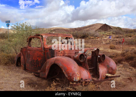 Old car rusting in Desert Landscape with Barn in Background Stock Photo