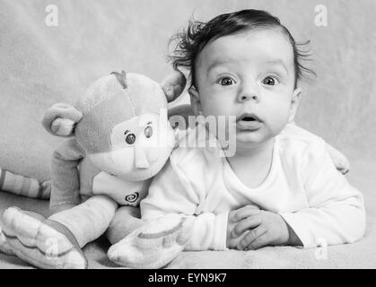 Portrait of an adorable smiling baby playing with a monkey toy. Stock Photo