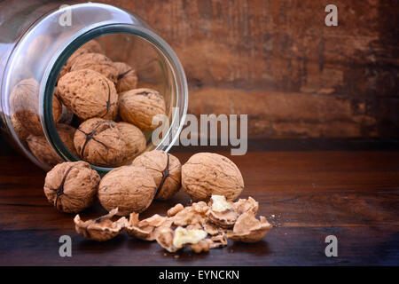 Fresh walnuts in shells falling out of glass jar on rustic dark wood table background. Stock Photo