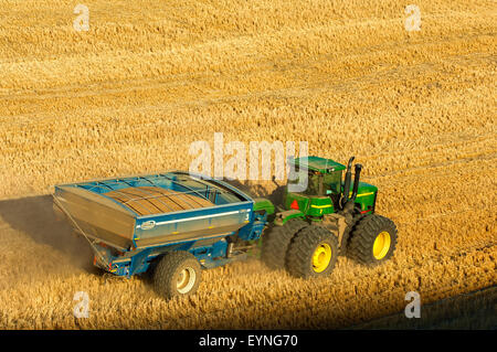 A tractor pulling  a loaded grain cart traverses a hillside field during harvest in the Palouse region of Washington Stock Photo