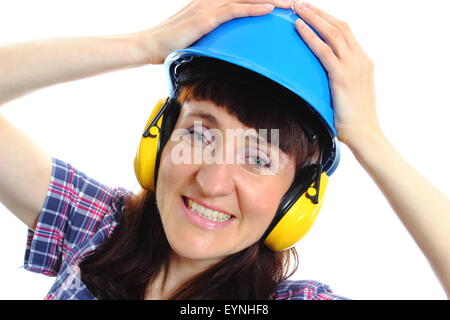 Shocked female construction worker wearing blue helmet and protective headphones, safety at work and ear protection. Stock Photo