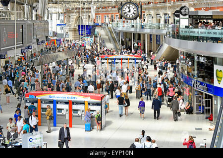 Commuters on Waterloo train station concourse with station clock self service train ticket machines retail shops & balconies London England UK Stock Photo