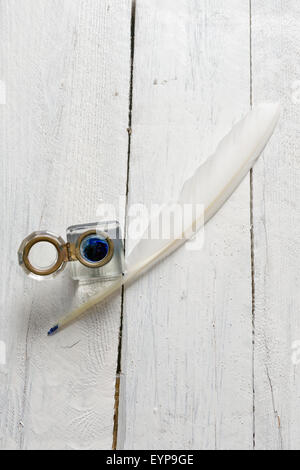 Feather quill and blue ink pot on a rustic white painted table Stock Photo