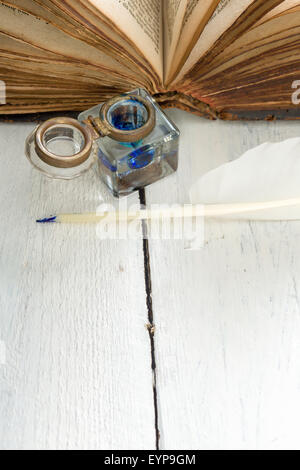 Feather quill, blue ink pot and medieval book on a rustic white painted table Stock Photo