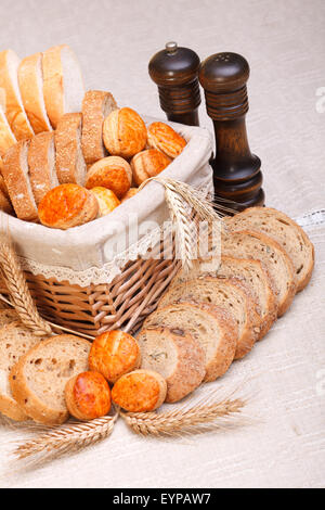 Assorted bakery products sliced, arranged in small basket. Wheat ears in front, salt and pepper behind Stock Photo