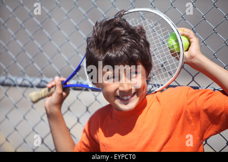 Young happy smiling boy outside in sun with tennis racket and ball Stock Photo