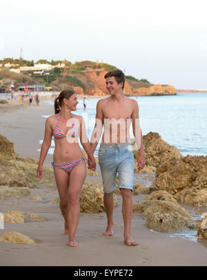Happy young couple walking on the beach between rocks and holding hands on a beach Stock Photo