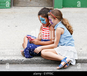Two young girls watching using a smart phone during public 4th of July celebration event in downtown Greensboro, North Carolina. Stock Photo