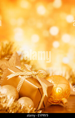 Golden Christmas baubles and a gift in front of defocused golden lights. Stock Photo