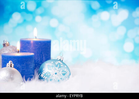 Blue and silver Christmas baubles and candles on a soft feathery surface in front of defocused blue and white lights. Stock Photo