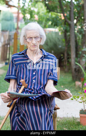 Ninety years old grandma reading the newspapers in the backyard Stock Photo