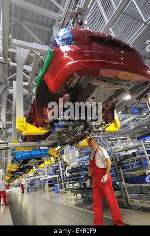 Inside a modern car factory, vehicles and parts move through the production process, workers below suspended cars Stock Photo