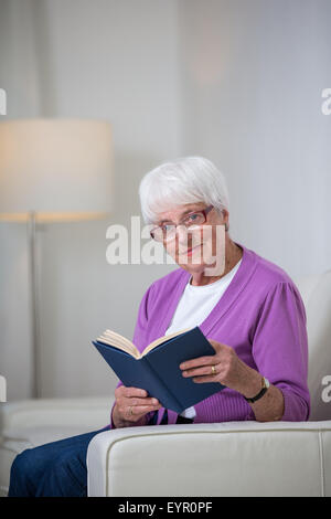 Portrait of a senior woman at home - Looking happy, looking at the camera, smiling while sitting on the sofa in her living room  Stock Photo