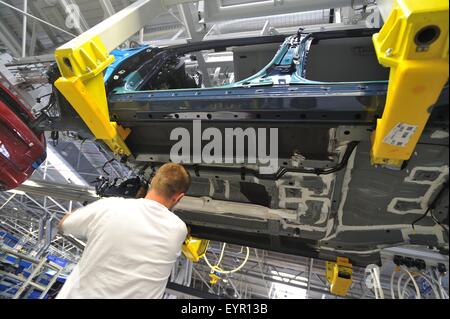 Inside a modern car factory, vehicles and parts move through the production process, worker under a car body shell Stock Photo