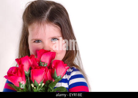 Young girl holding a bunch of artifiical roses smelling them. Looking at the camera and lots of copy space. Stock Photo