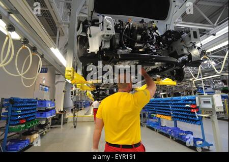 Inside a modern car factory, vehicles and parts move through the production process, workers under the raised car running gear Stock Photo