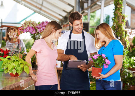 Gardener in a nursery shop giving advice to two female customers Stock Photo