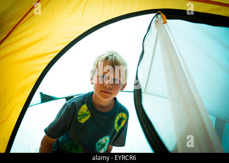 Child blond boy peeking, looking, poking into tent out of zipped entrance Stock Photo