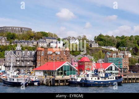 Boats moored by the pier with McCaig's tower folly on hill above in Oban, Argyll and Bute, Scotland, UK, Britain Stock Photo