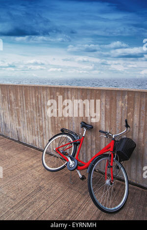 Classic Vintage Red Bicycle Leaning Against Concrete Wall, Sea and Clouds in Background, Retro Toned Image Stock Photo