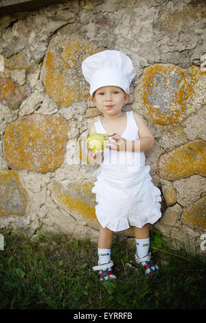 little boy with chefs hat eats apple Stock Photo