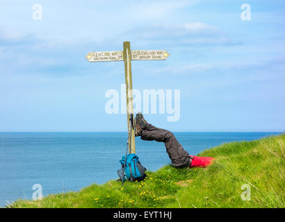 Male hiker resting with feet on signpost at Skinningrove between Saltburn and Staithes on The Cleveland Way trail. UK Stock Photo
