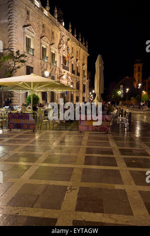 Outdoor restaurant tables at Plaza Nueva and Santa Ana at night with Royal Chancery of Granada