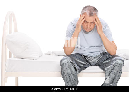 Frustrated senior sitting on a bed in his pajamas and looking down isolated on white background Stock Photo