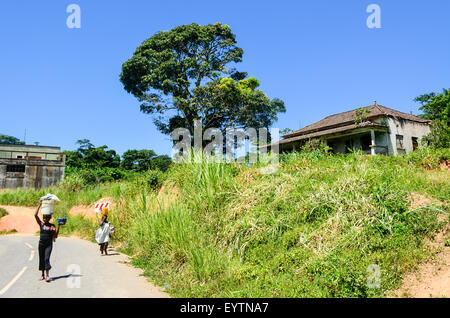 Two women carrying bags on their head on the road by an abandoned house in Angola Stock Photo