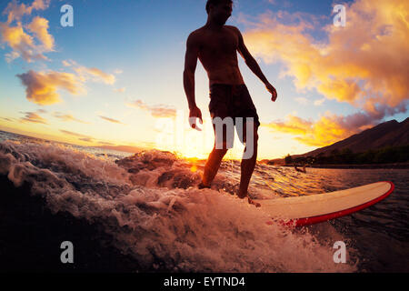 Surfing at Sunset. Young Man Riding Wave at Sunset. Outdoor Active Lifestyle. Stock Photo