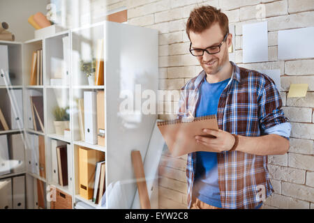 Smiling businessman in casualwear making notes or drawing sketch by office wall Stock Photo